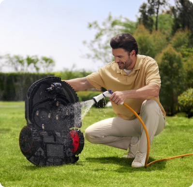 Man cleaning lawn mower with hose